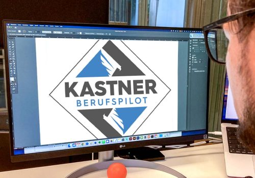 Man sieht über die Schultern von einem Mann mit Brill und schwarzen Haaren auf einen Bildschirm. Auf dem Bildschirm sieht man das Logo von Berufspilot Kevin Kastner